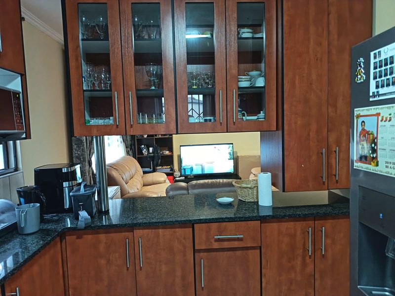 A functional kitchen featuring dark wood cabinetry, granite countertops, and glass-front display units, with an open-plan layout overlooking the living area.