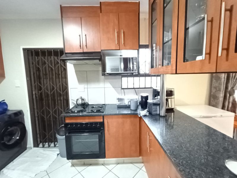 A functional kitchen featuring wooden cabinetry, granite countertops, a built-in oven and stove, and tiled flooring, with an adjacent security gate.
