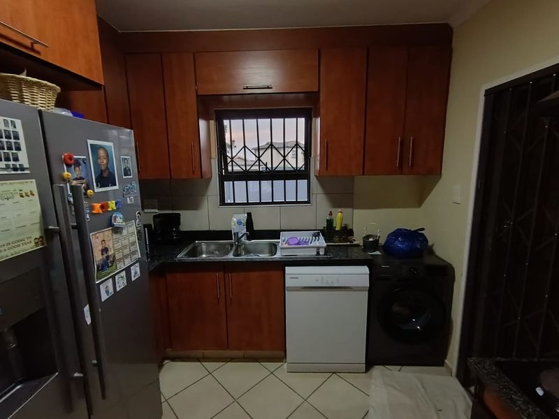 A functional kitchen featuring wooden cabinetry, granite countertops, a double basin sink, and tiled flooring with security bars on the window.