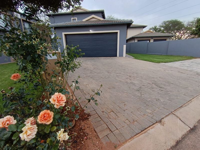 Front view of the property featuring a paved driveway, automated garage door, and well-maintained boundary wall with landscaped garden area.