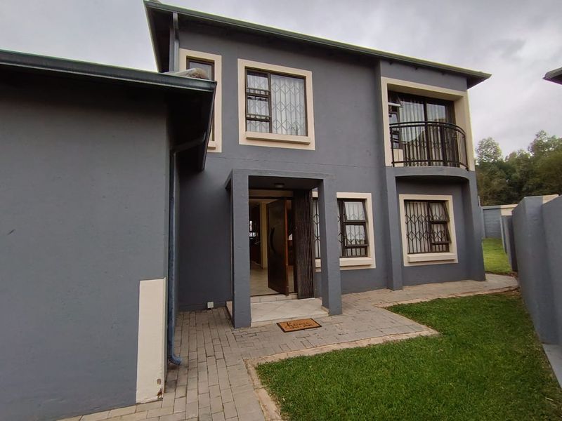 Rear view of a two-story house featuring a paved patio area, a small balcony, and secure window grilles.