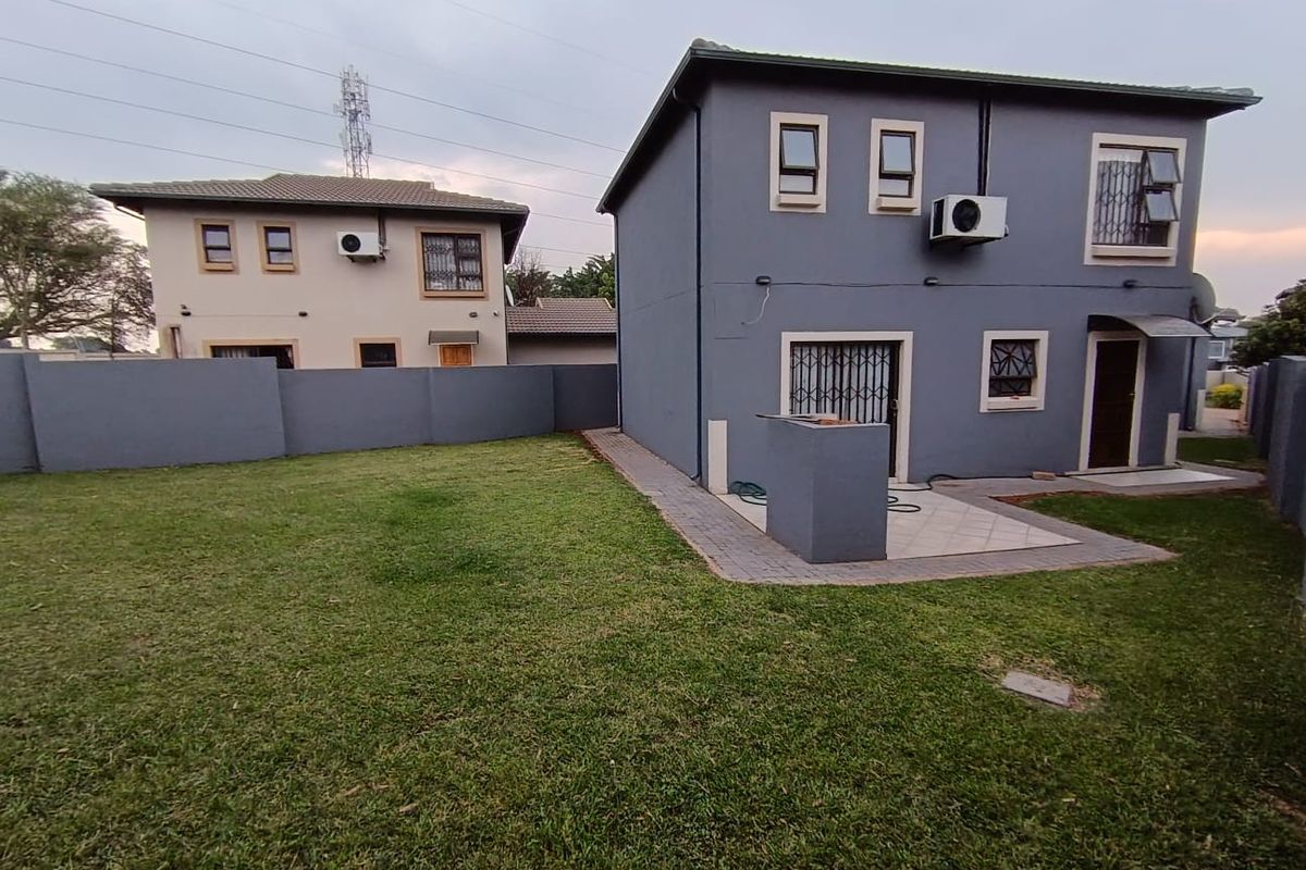 Rear view of the property featuring a paved patio area, built-in braai, security gates, and a private garden enclosed by boundary walls.