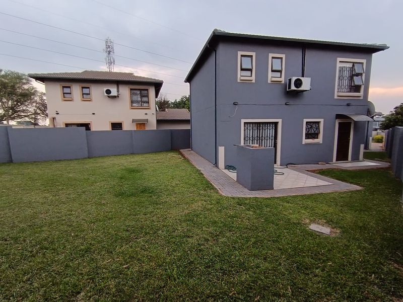 Rear view of the property featuring a paved patio area, built-in braai, security gates, and a private garden enclosed by boundary walls.