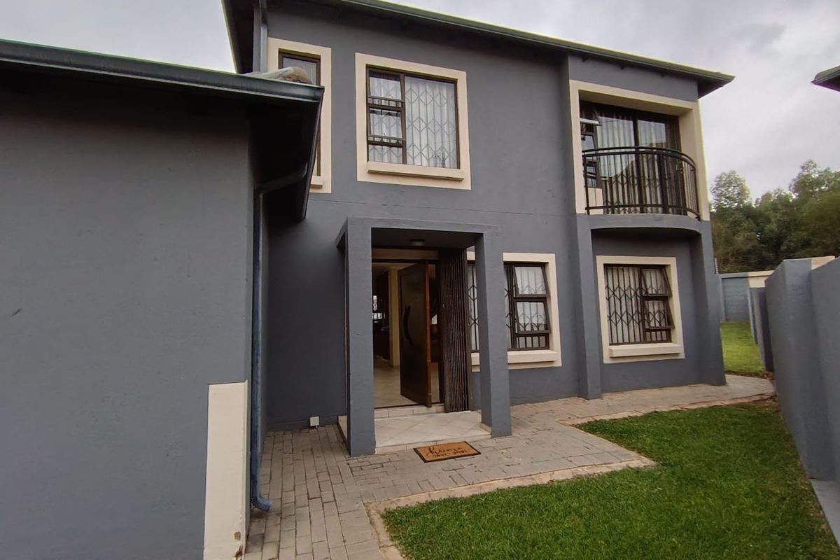 Rear view of a two-story house featuring a paved patio area, a small balcony, and secure window grilles.