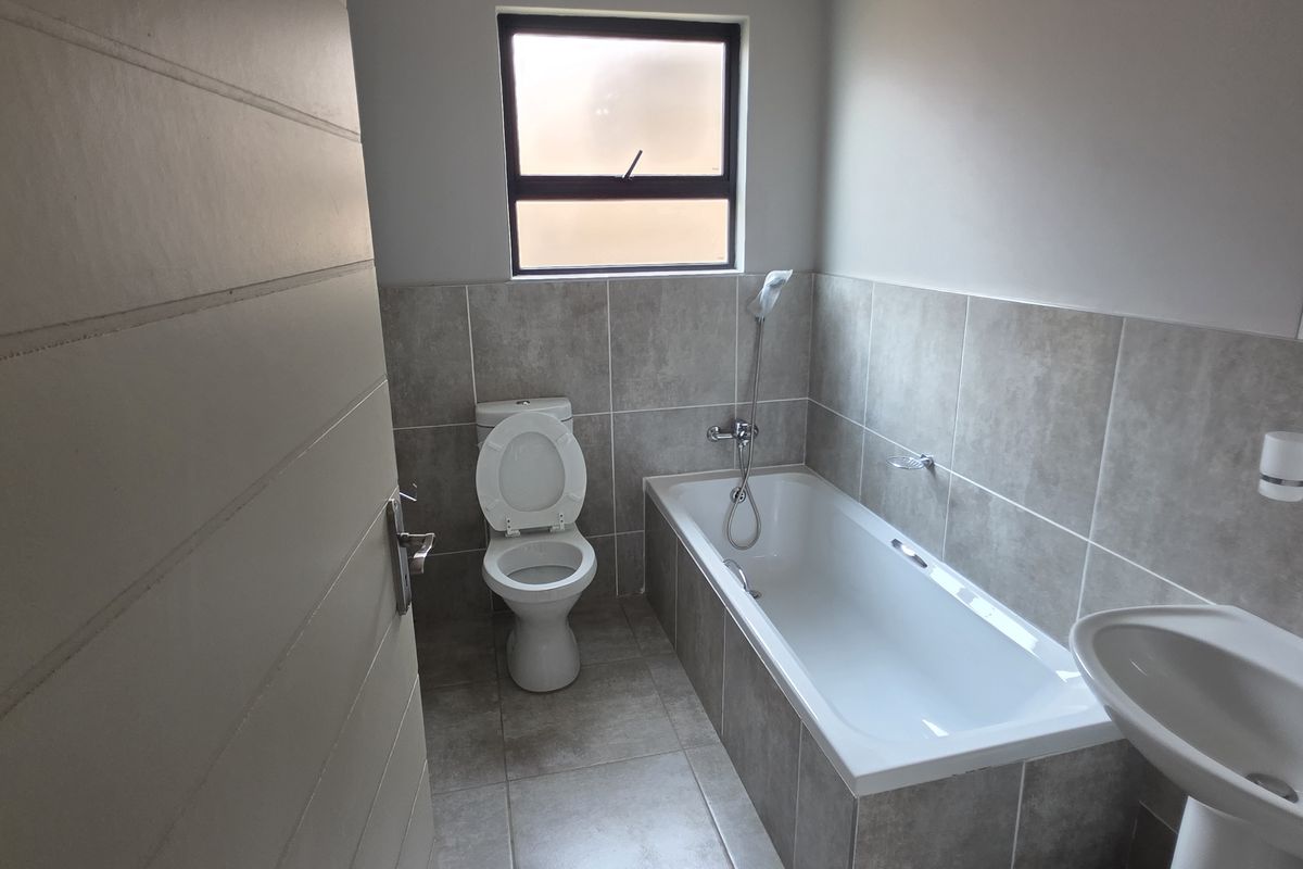 A functional bathroom featuring a bathtub with a handheld shower attachment, a pedestal basin, and a toilet, finished with neutral wall and floor tiling.