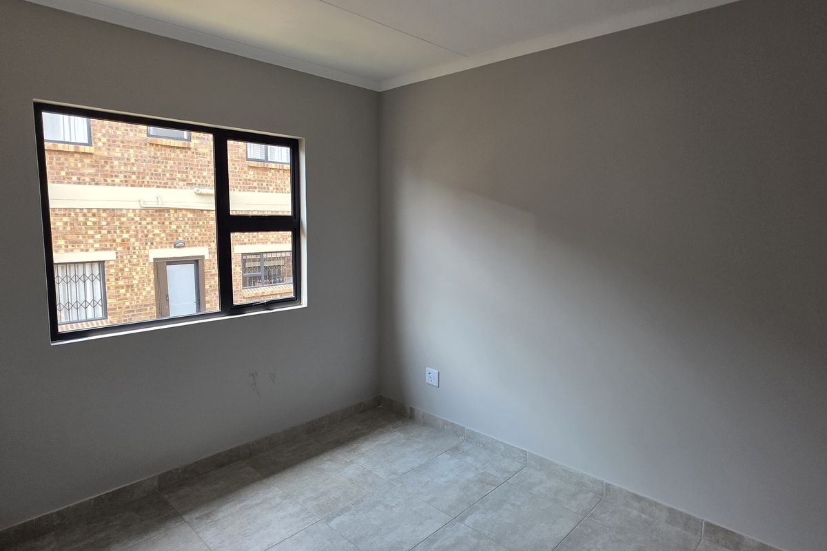 A clean, empty bedroom featuring neutral wall paint, tiled flooring, and a window providing natural light.