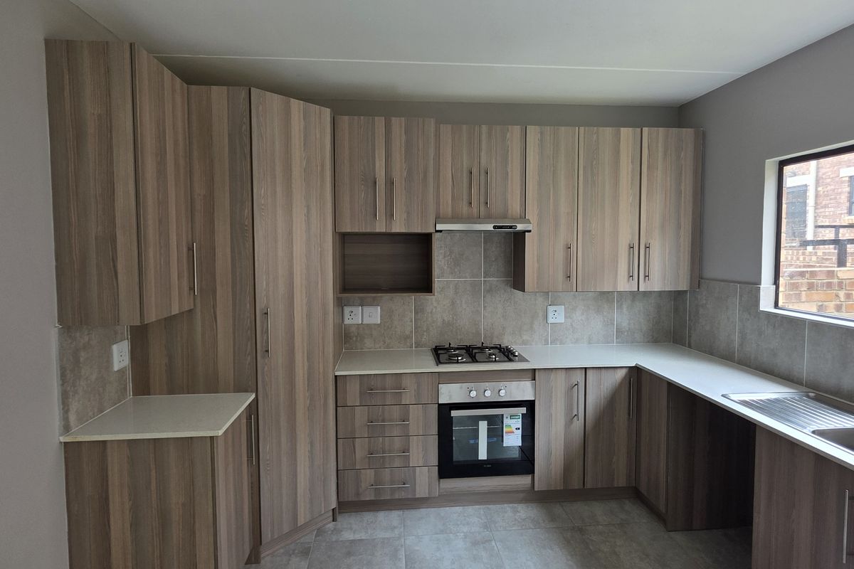 Modern kitchen featuring wood-grain cabinetry, stone-look countertops, built-in gas hob, oven, extractor fan, and a double stainless steel sink.