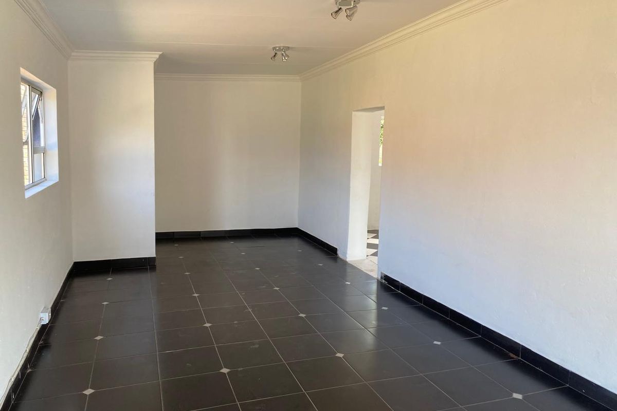 A bright, empty living area featuring dark ceramic floor tiles with decorative inserts, white walls, and modern ceiling-mounted spotlights.