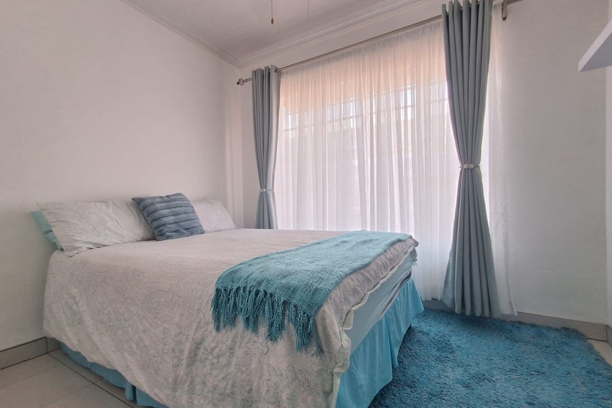 A bright bedroom featuring tiled flooring, neutral walls, and large windows dressed with floor-to-ceiling curtains.