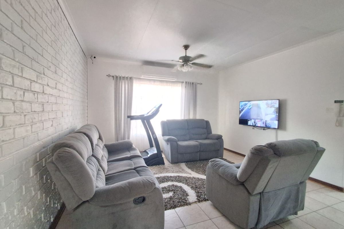 A living room featuring a white painted brick accent wall, tiled flooring, and a ceiling fan.
