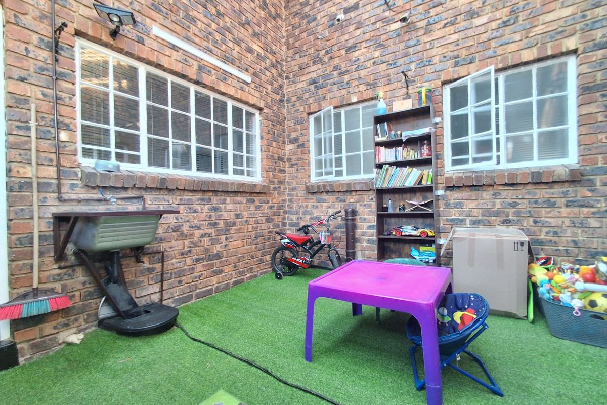 A private rear courtyard featuring exposed brick walls, artificial turf flooring, and a wall-mounted utility sink.