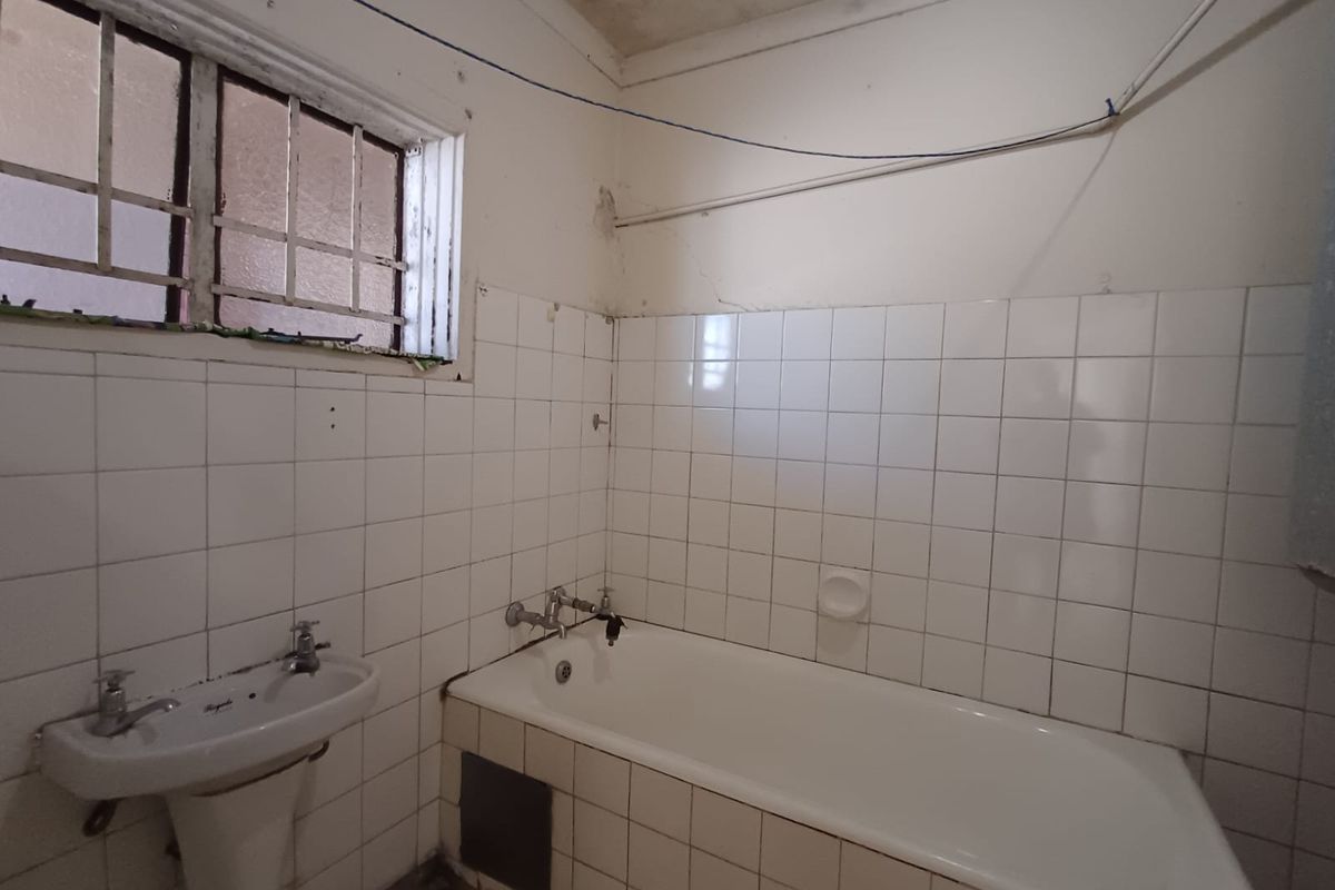 A dated bathroom featuring a standard bathtub, pedestal basin, and tiled walls, requiring significant renovation and cosmetic updates.