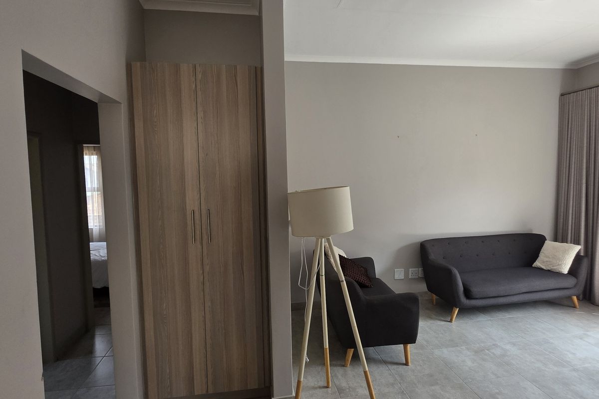 A living room featuring neutral wall tones, large floor tiles, and a built-in wooden cupboard, with access to an adjoining room.