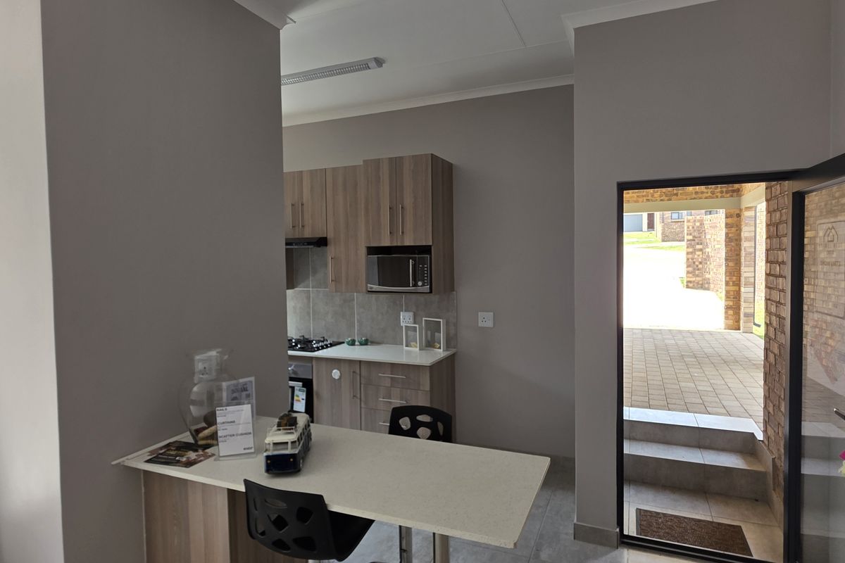 A compact kitchen featuring modern wood-look cabinetry, built-in hob and oven, and a breakfast bar, with direct access to an outdoor patio area.