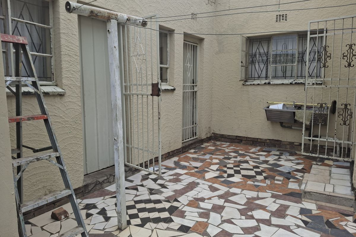 Rear courtyard area featuring a utility sink, security gates, and patterned tiled flooring, requiring maintenance and cosmetic updates to improve the outdoor space.