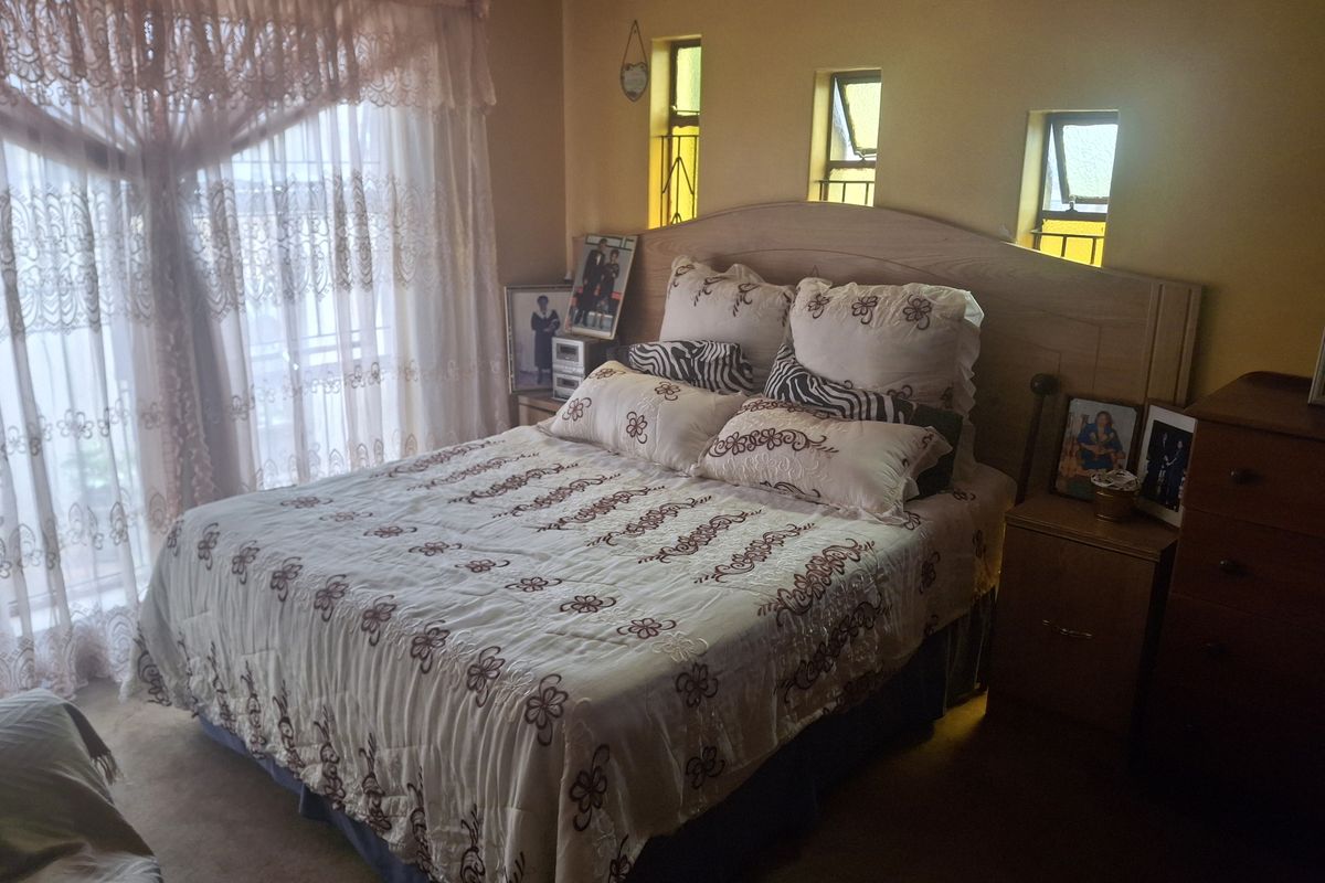 A bedroom featuring a built-in headboard, multiple small casement windows with security bars, and large sliding glass doors with curtains.