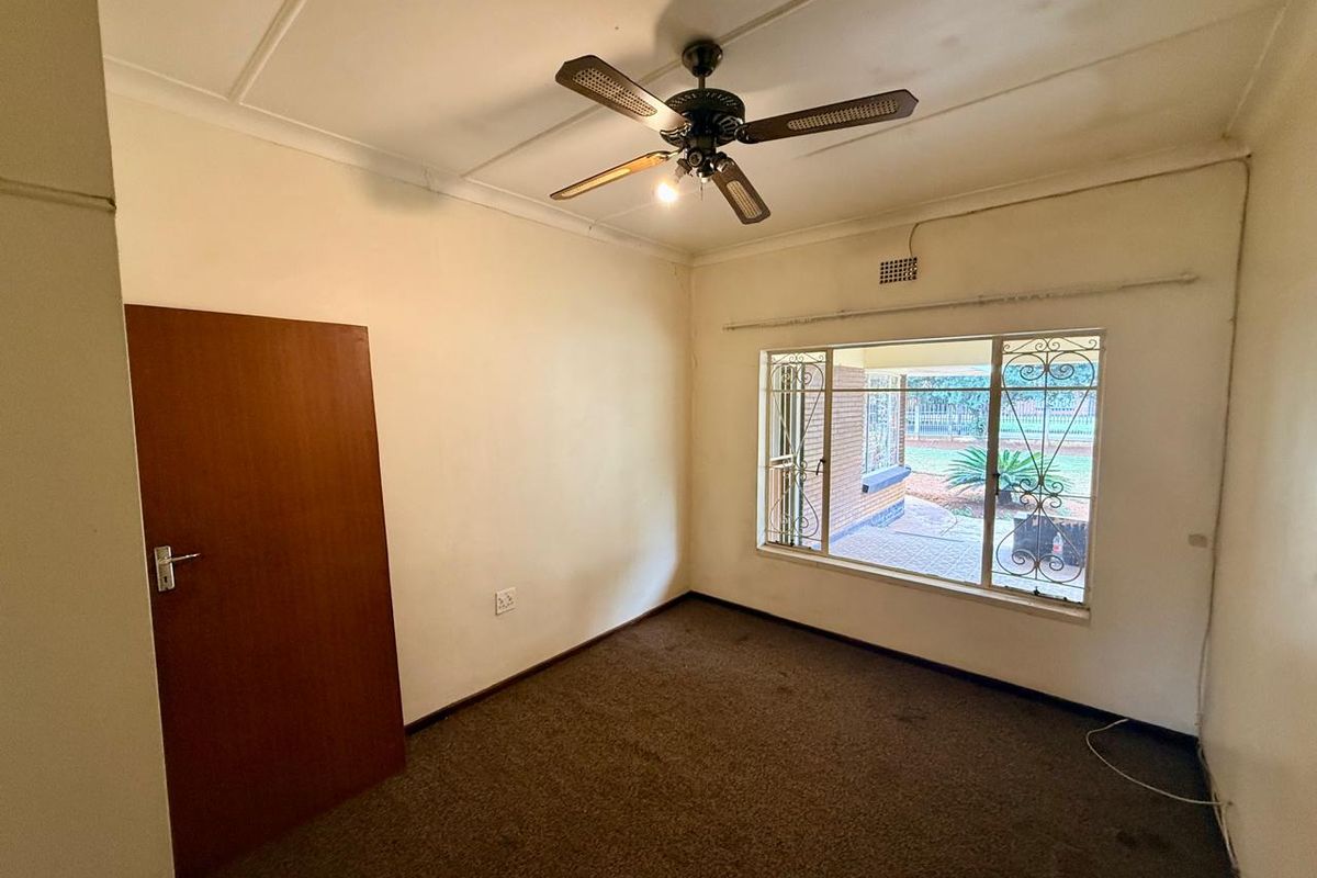 A vacant bedroom featuring a ceiling fan, carpeted flooring, and a window with security bars overlooking the exterior.