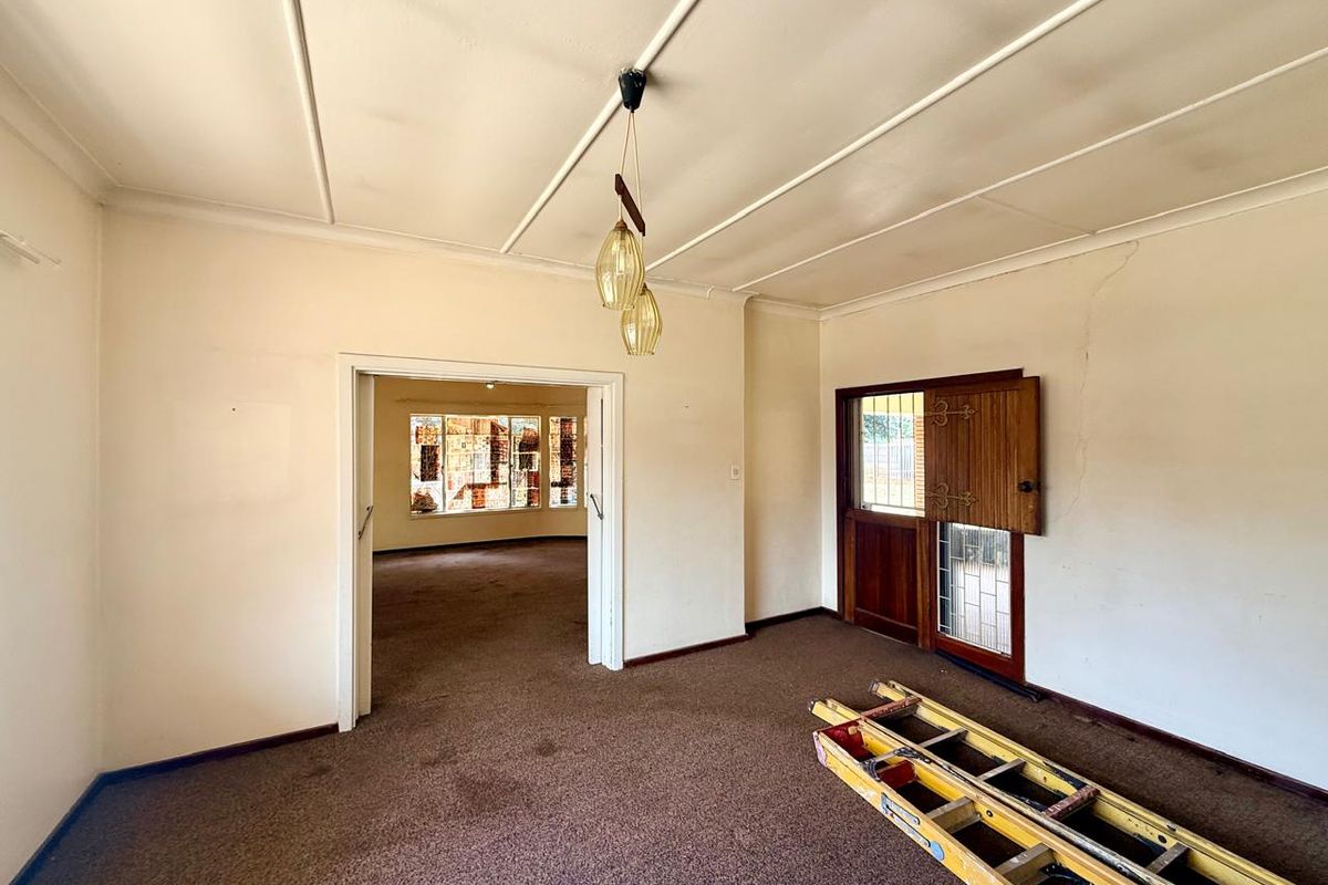 A dated living room featuring a stable-style wooden door, carpeted flooring, and a view through to an adjacent room with decorative window detailing.