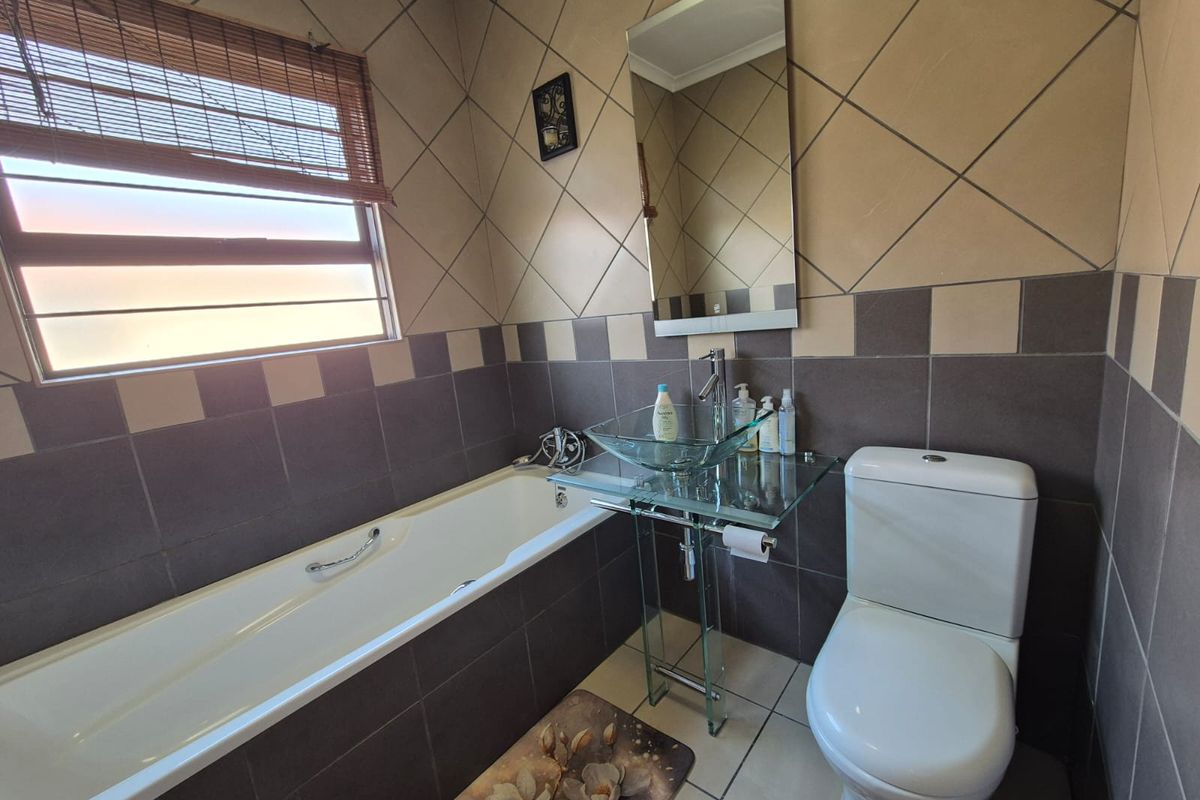 A compact bathroom featuring a built-in bathtub, a glass vessel sink with a pedestal vanity, and a standard toilet with tiled walls.