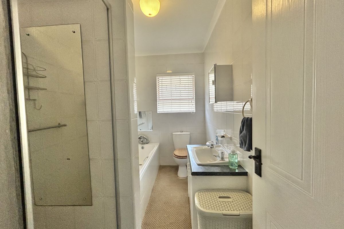 A functional bathroom featuring a built-in bathtub, shower enclosure, vanity with basin, and toilet, finished with neutral wall tiles.