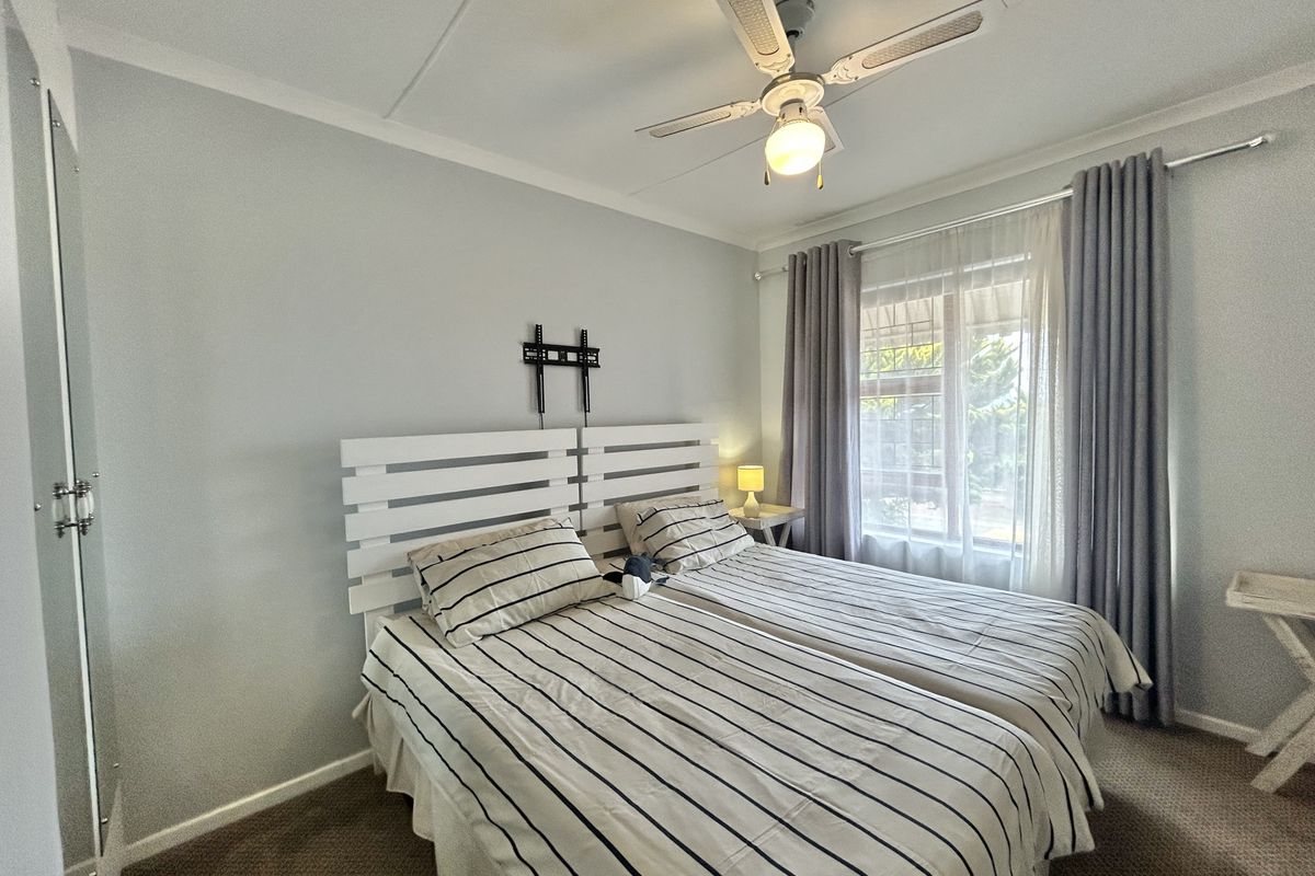 A well-lit bedroom featuring a ceiling fan, carpeted flooring, and a window with curtain tracks.