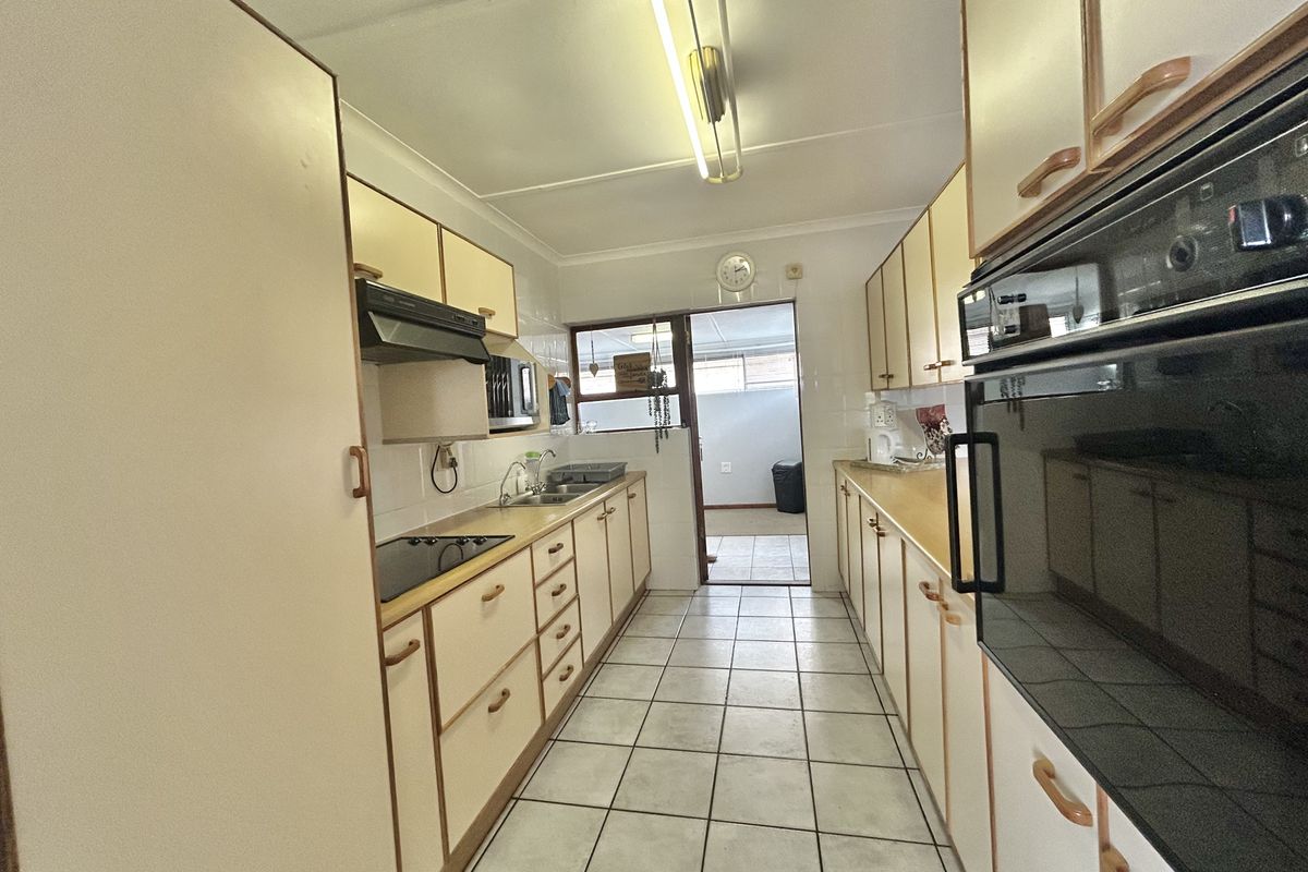 A galley-style kitchen featuring built-in cabinetry, a double sink, integrated oven, and hob, with tiled flooring leading to an adjacent room.