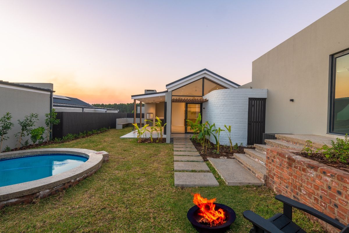 A beautifully landscaped rear garden featuring a swimming pool, a covered patio with a built-in braai, and modern architectural finishes.