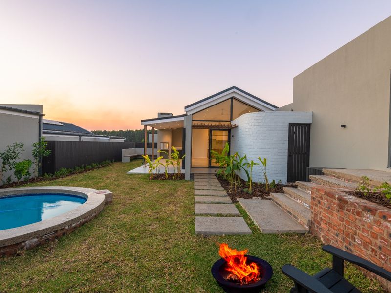 A beautifully landscaped rear garden featuring a swimming pool, a covered patio with a built-in braai, and modern architectural finishes.