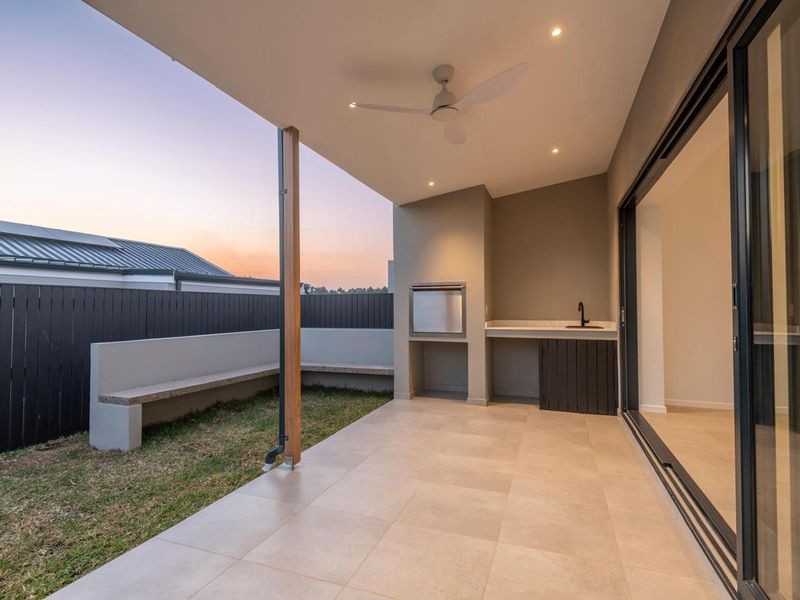 A modern covered patio featuring a built-in braai, outdoor sink, tiled flooring, and a built-in bench, seamlessly connecting to the interior living space.