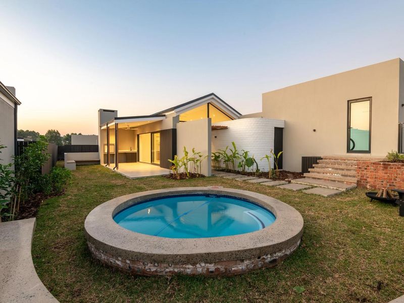Modern rear exterior featuring a circular plunge pool, covered patio with built-in braai, and landscaped garden area with contemporary architectural finishes.