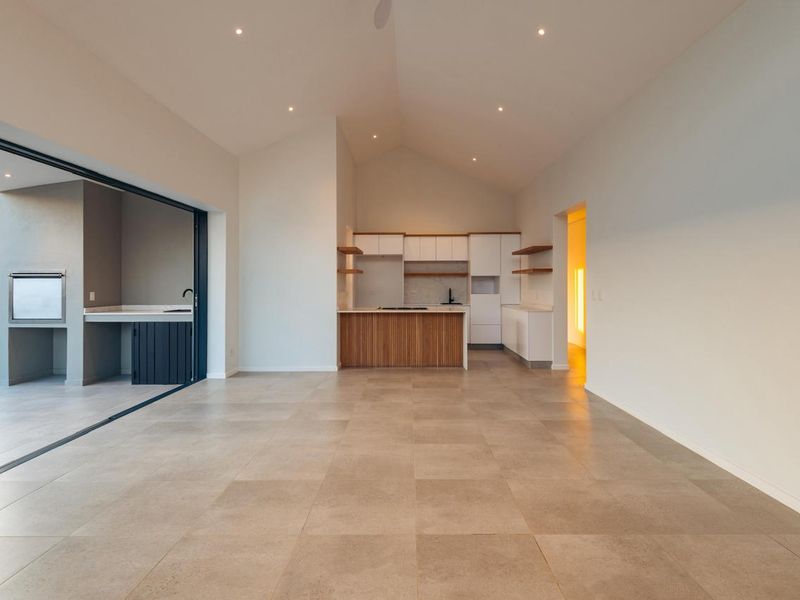 Spacious open-plan living area featuring a modern kitchen with built-in cabinetry, vaulted ceilings, and seamless flow to an outdoor patio with a built-in braai.
