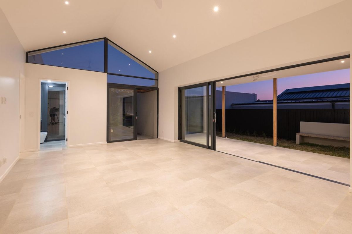 Spacious, modern living area featuring vaulted ceilings, large sliding glass doors opening to a patio, and neutral tiled flooring throughout.