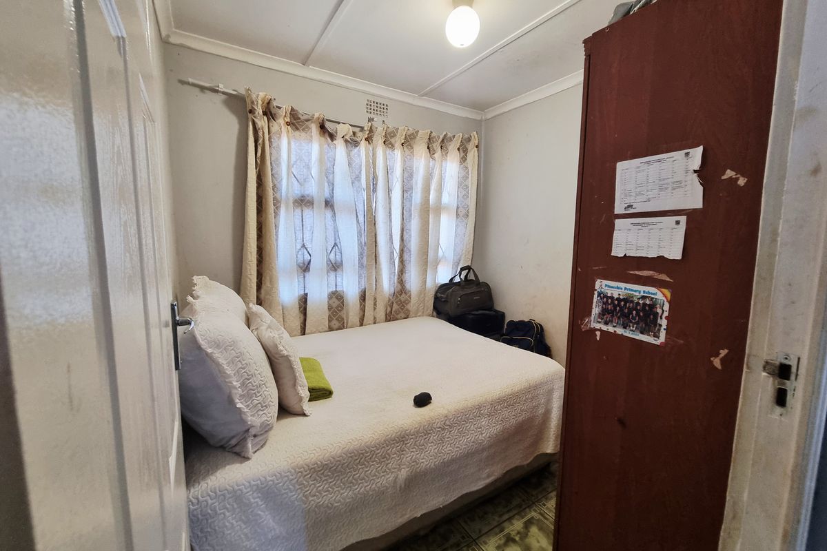 A compact bedroom featuring tiled flooring, a built-in cupboard, and a window with curtain fixtures.