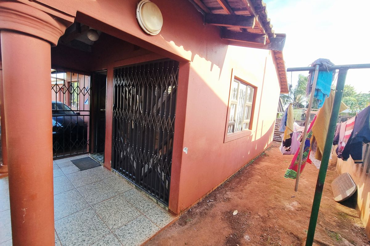 Side view of the house featuring a covered patio area with security gates and tiled flooring, adjacent to an open garden space.