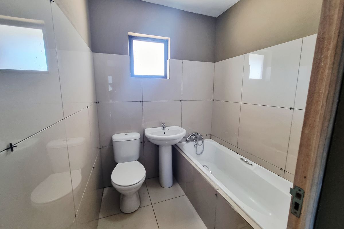 A functional bathroom featuring a white pedestal basin, toilet, and a built-in bathtub with tiled surround and walls.