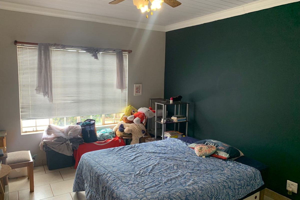 A bedroom featuring tiled flooring, a ceiling fan, and a dark green accent wall with natural light provided by a large window.