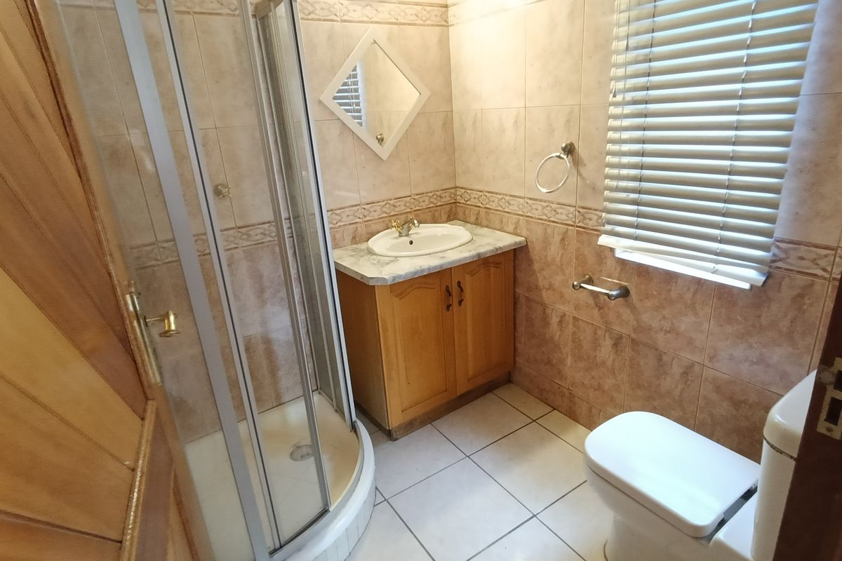 A compact bathroom featuring a corner shower enclosure, a vanity with a marble-effect countertop, and tiled walls and flooring.