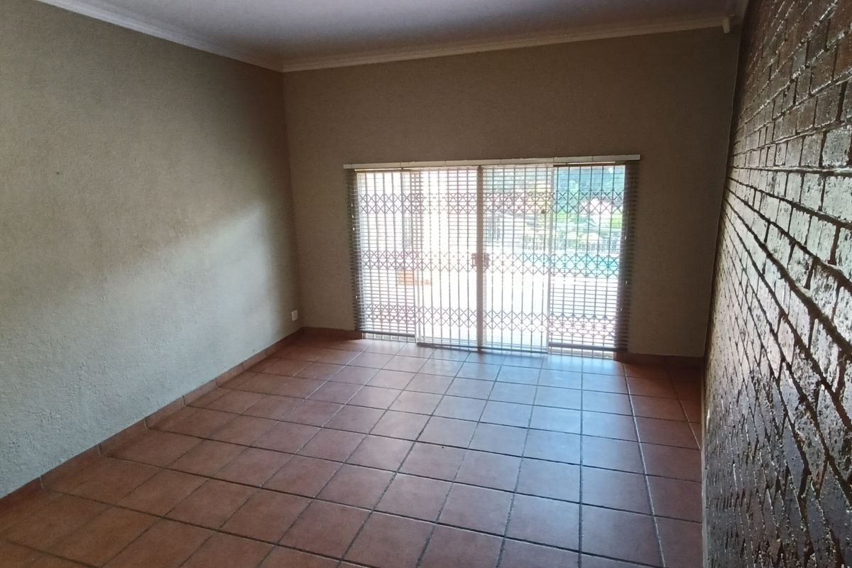 An empty living room featuring terracotta floor tiles, a textured brick feature wall, and sliding glass doors with security gates leading outdoors.