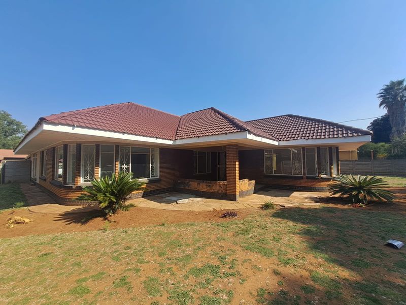 A rear view of a single-story brick house featuring a tiled roof, security-barred windows, and a paved patio area overlooking a garden.