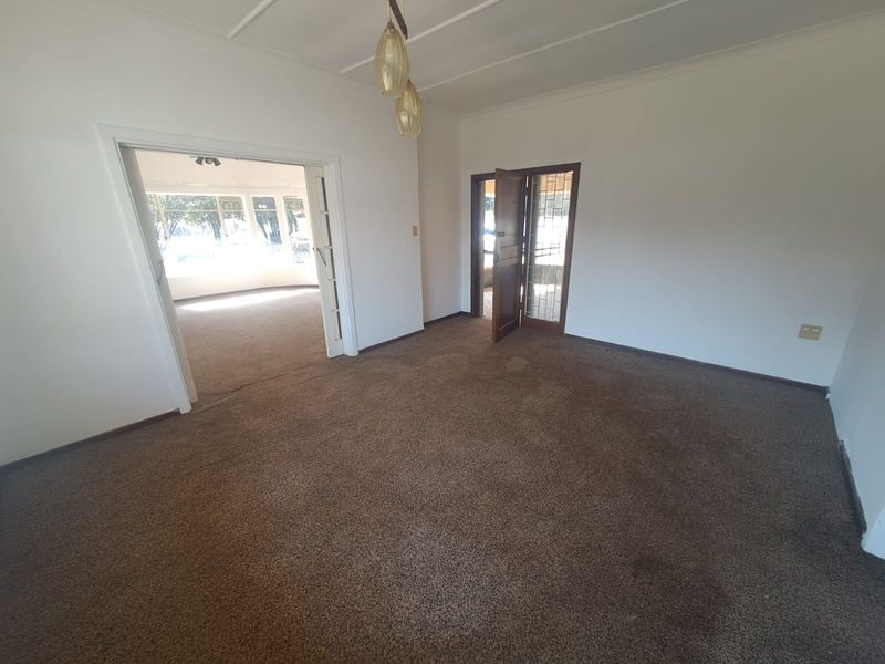 An empty living room featuring carpet flooring, coved ceilings, and access to an adjoining sunroom through a wide doorway.