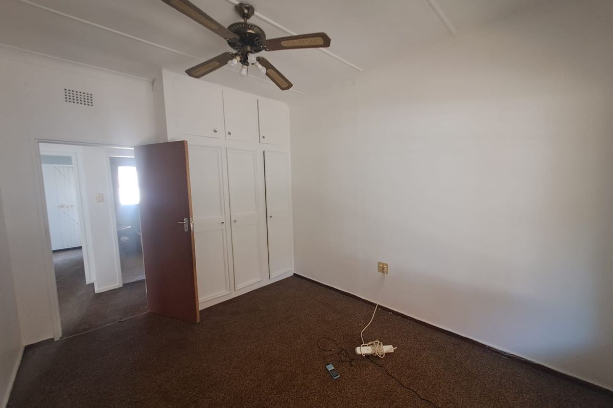 A vacant bedroom featuring built-in cupboards, a ceiling fan, and carpeted flooring, offering a blank canvas for renovation.