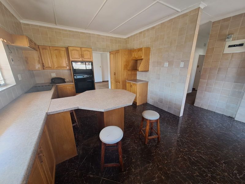 A functional kitchen featuring wooden cabinetry, laminate countertops, built-in oven, and tiled finishes throughout, offering a classic layout with potential for modern updates.