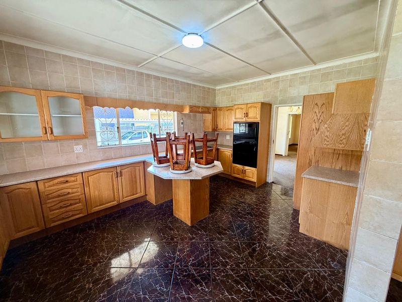 A functional kitchen featuring traditional wooden cabinetry, tiled backsplash, built-in oven, and dark marble-effect floor tiles, offering potential for modern updates.