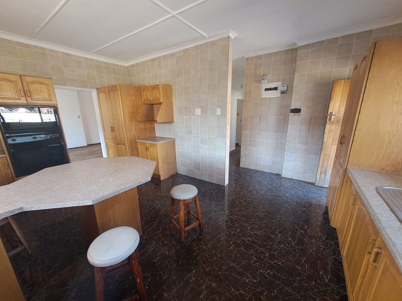 A functional kitchen featuring wooden cabinetry, tiled walls, and a central breakfast counter, offering a dated but well-maintained layout.