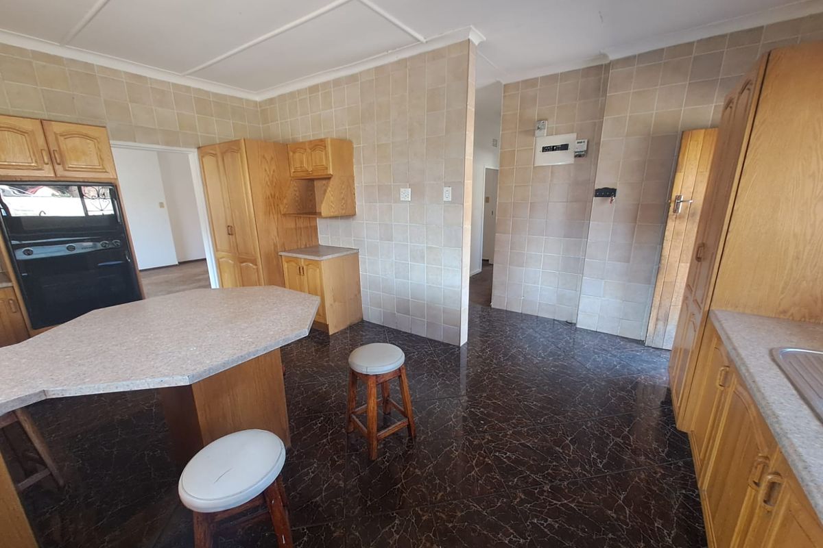 A functional kitchen featuring wooden cabinetry, tiled walls, and a central breakfast counter, offering a dated but well-maintained layout.