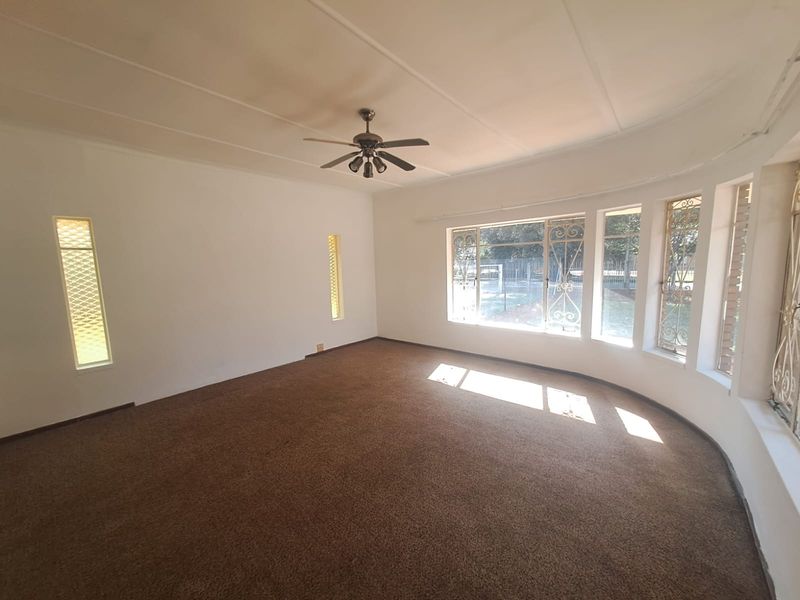 Spacious living area featuring large windows with security bars, a ceiling fan, and carpeted flooring, offering a bright and open layout.