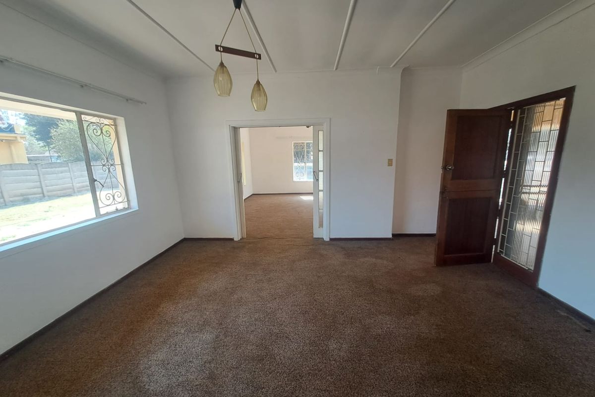 An empty living room featuring worn carpet flooring, a timber door with security gate, and decorative ceiling molding.