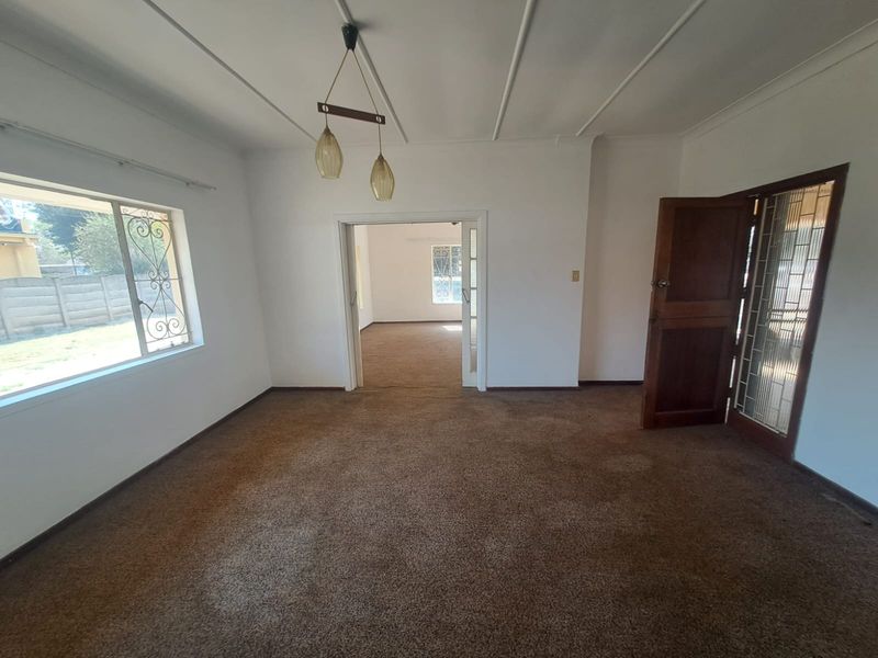An empty living room featuring worn carpet flooring, a timber door with security gate, and decorative ceiling molding.