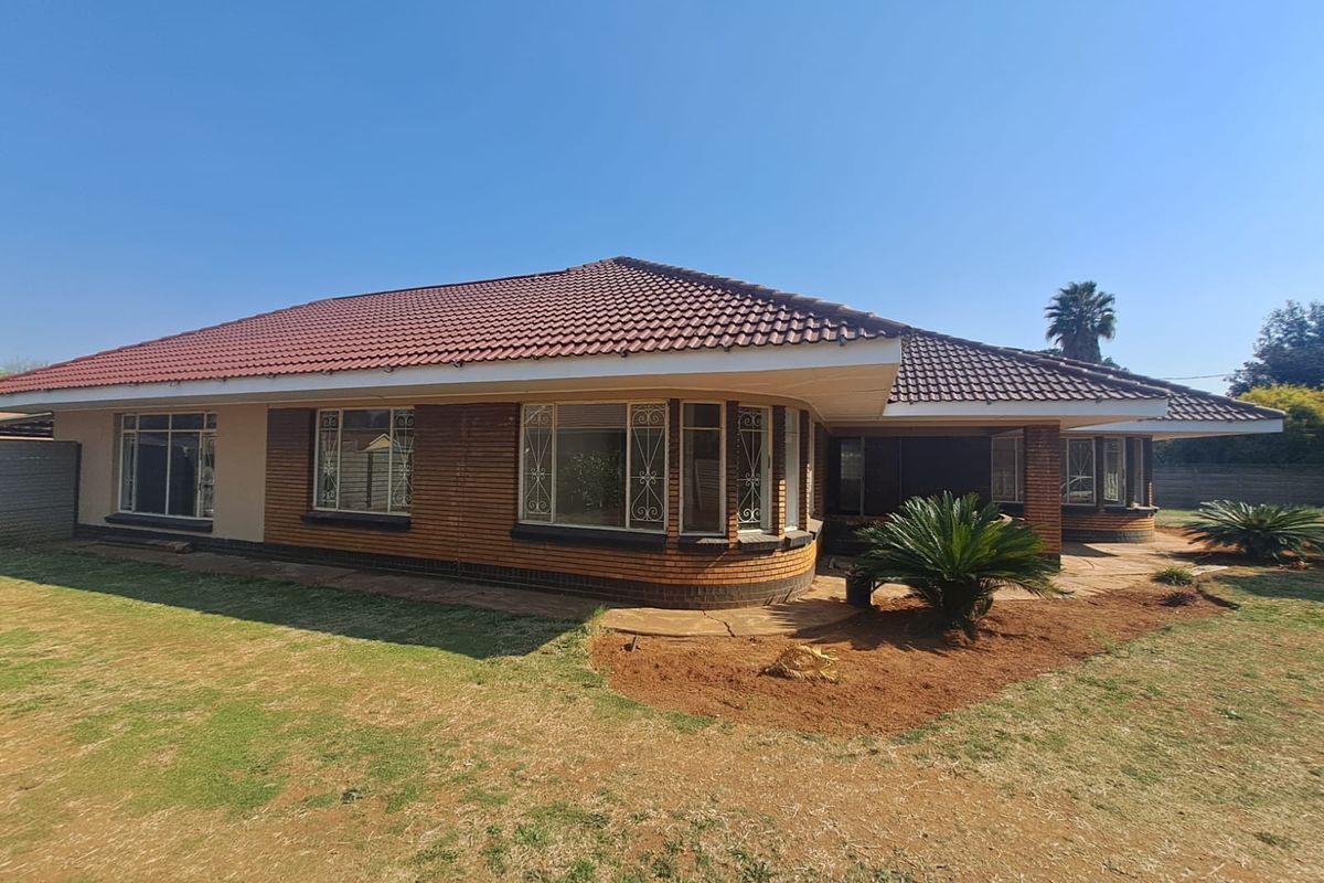 Rear view of a single-story brick house featuring a tiled roof, bay windows with security bars, and a paved patio area overlooking the garden.
