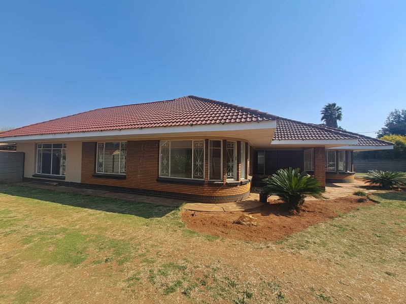 Rear view of a single-story brick house featuring a tiled roof, bay windows with security bars, and a paved patio area overlooking the garden.